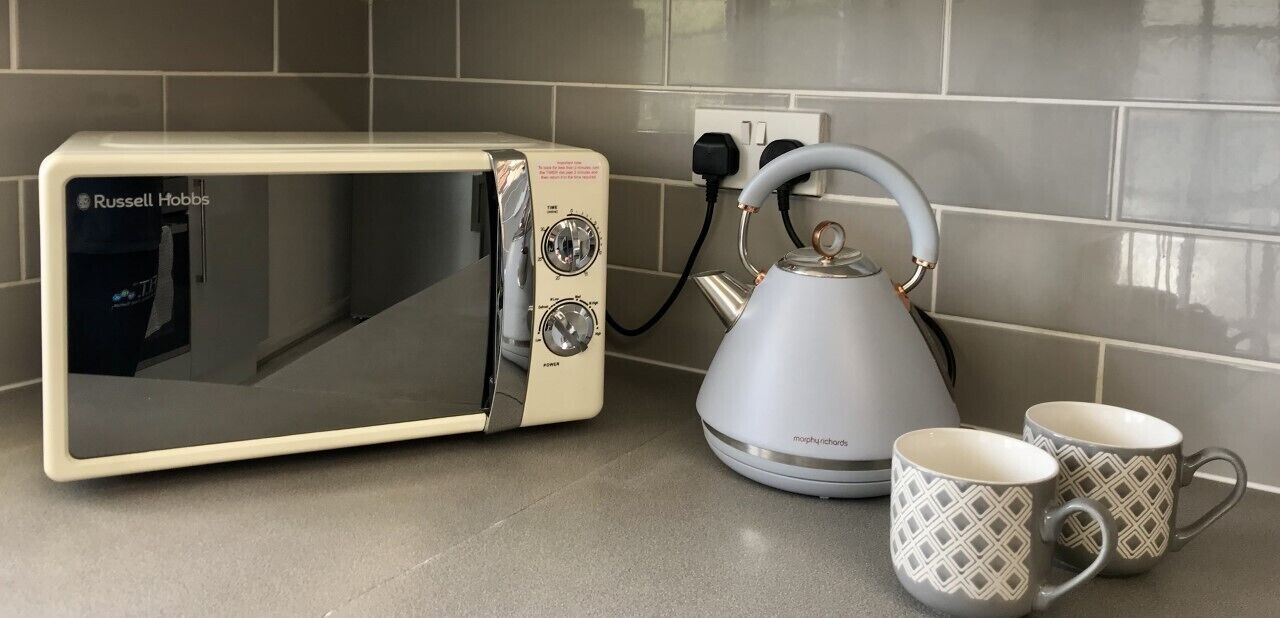 A kitchen with a white Russell Hobbs microwave, a kettle, and two patterned mugs on the counter.