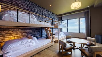 Ett modernt hotellrum med en våningssäng, en bäddsoffa, ett matbord och utsikt över havet.