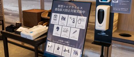 A display of a new touchless hand sanitizer dispenser, a sign with instructions, and a wooden table with a basket and a box.