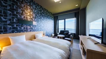 Habitación de hotel con dos camas grandes, zona de estar con vista al mar, televisión de pantalla plana y pared con diseño de piedra.