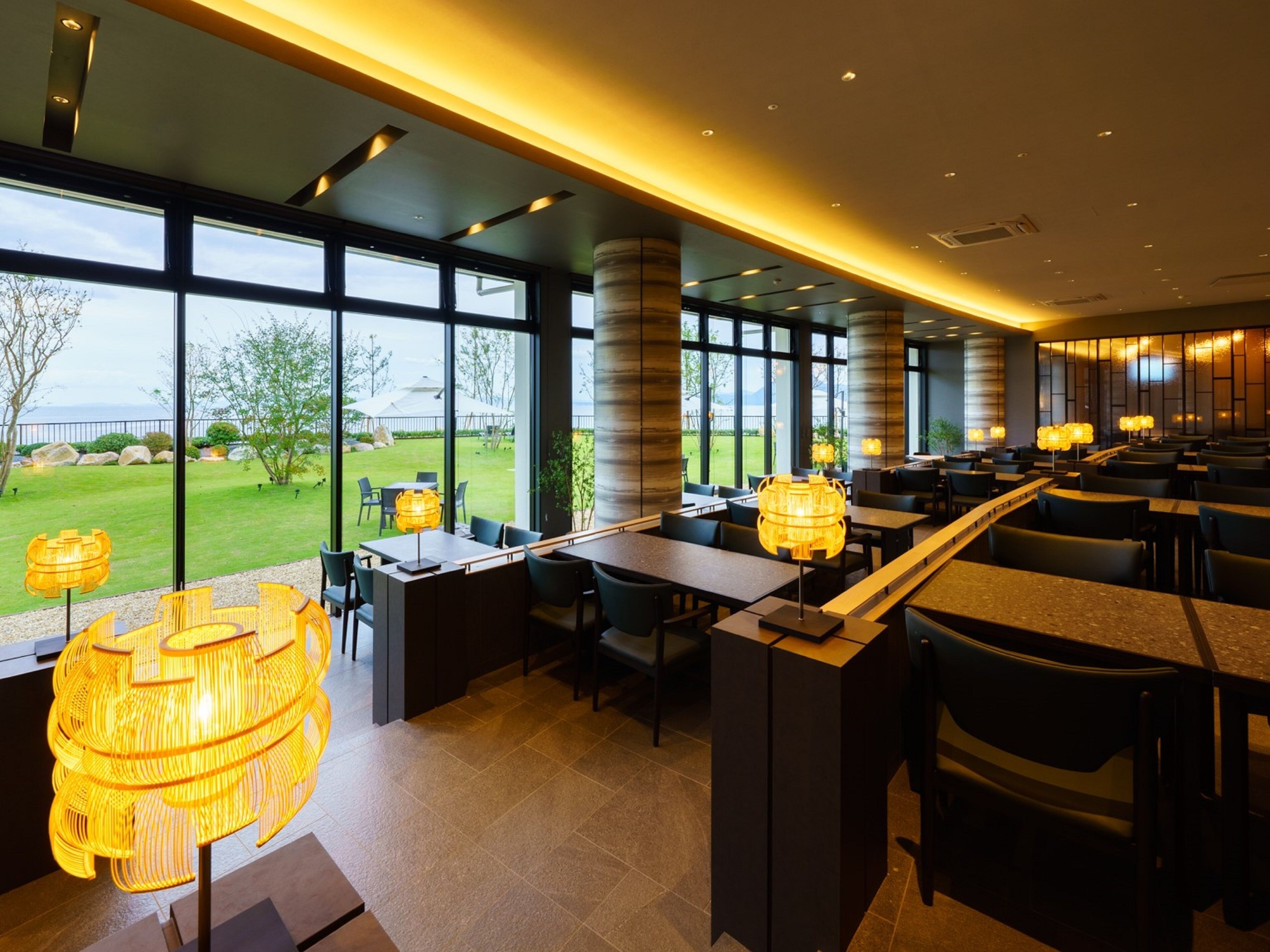 A modern restaurant with large windows, outdoor seating, and stylish lighting fixtures.