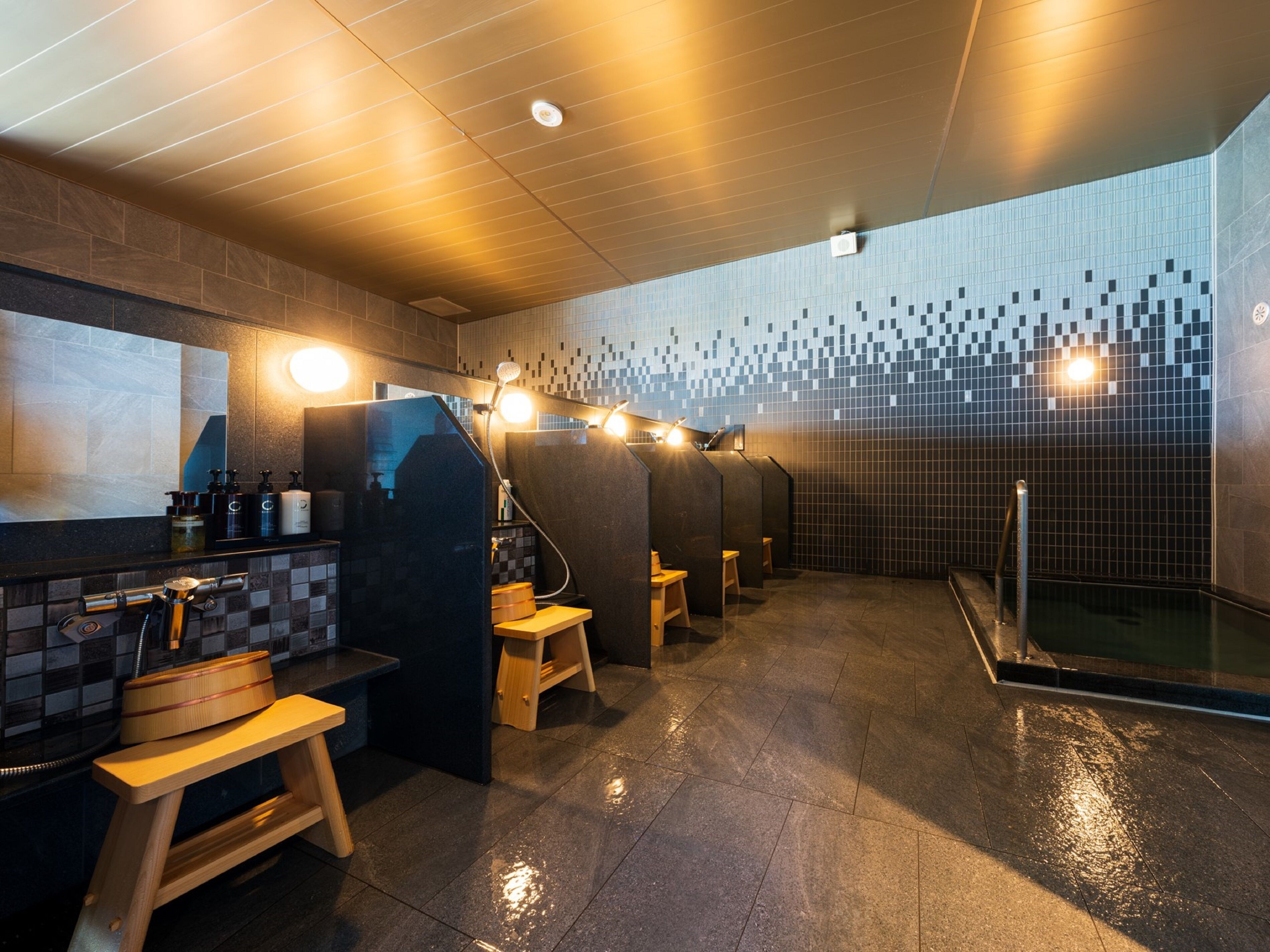 Un baño moderno con suelo de baldosas, un banco de madera, zona de lavamanos con artículos de aseo y cabina de ducha.