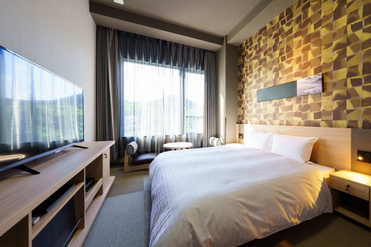Een moderne hotelkamer met een groot bed, een flatscreen televisie, een bureau en een zithoek met uitzicht op de omgeving.