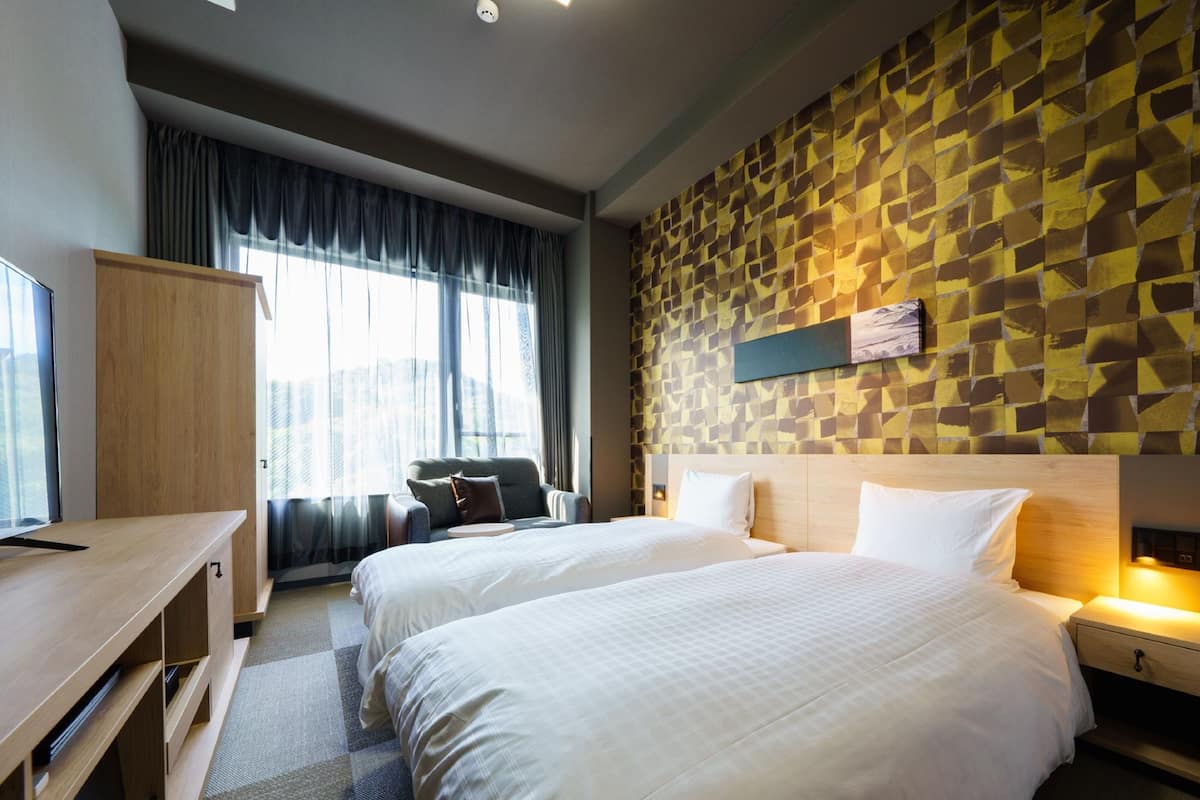 Een hotelkamer met twee bedden, een bureau, een kledingkast en een groot raam met gordijnen.