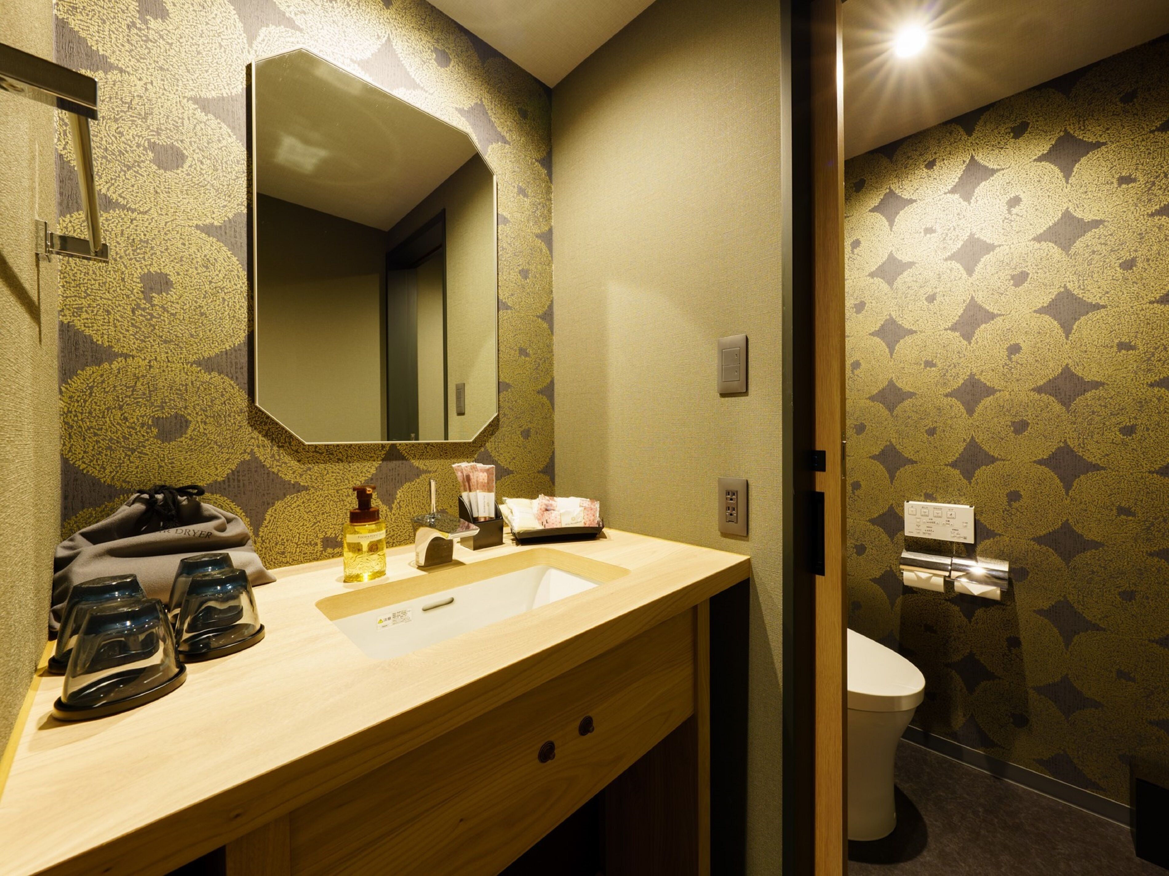 A bathroom with a wooden vanity, a mirror, a sink, and a toilet. There are toiletries on the vanity.