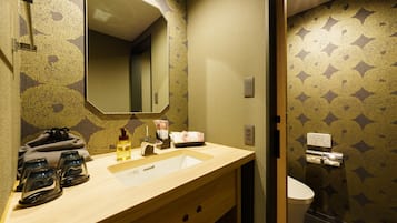 A bathroom with a wooden vanity, a mirror, a sink, and a toilet. There are toiletries on the vanity.