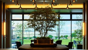 Un hall d’entrée moderne, agrémenté d’un grand arbre en pot, de sièges confortables et de grandes fenêtres offrant une vue sur l’extérieur.