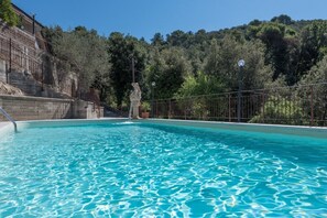 Une piscine à l’eau d’un bleu cristallin, entourée d’un mur de pierre et d’une clôture en métal.