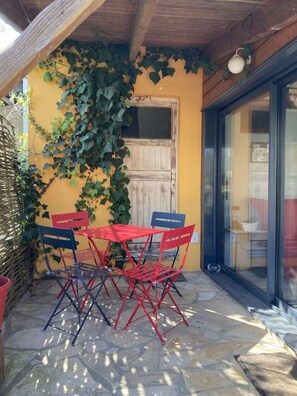Un patio con una mesa y sillas, techo de madera y pared amarilla cubierta de hiedra.