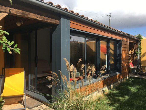 A modern house with large windows, a wooden exterior, and a garden area with tall grasses.