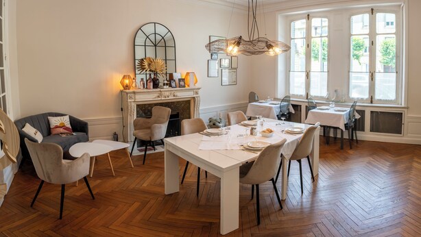A dining area with a white table set for four, surrounded by chairs, a fireplace, and a large window with natural light.