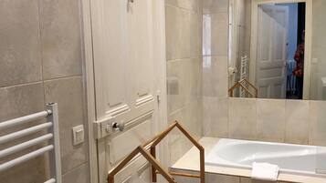 Un baño moderno con bañera, cabina de ducha de vidrio y una toalla blanca colgada en la bañera.