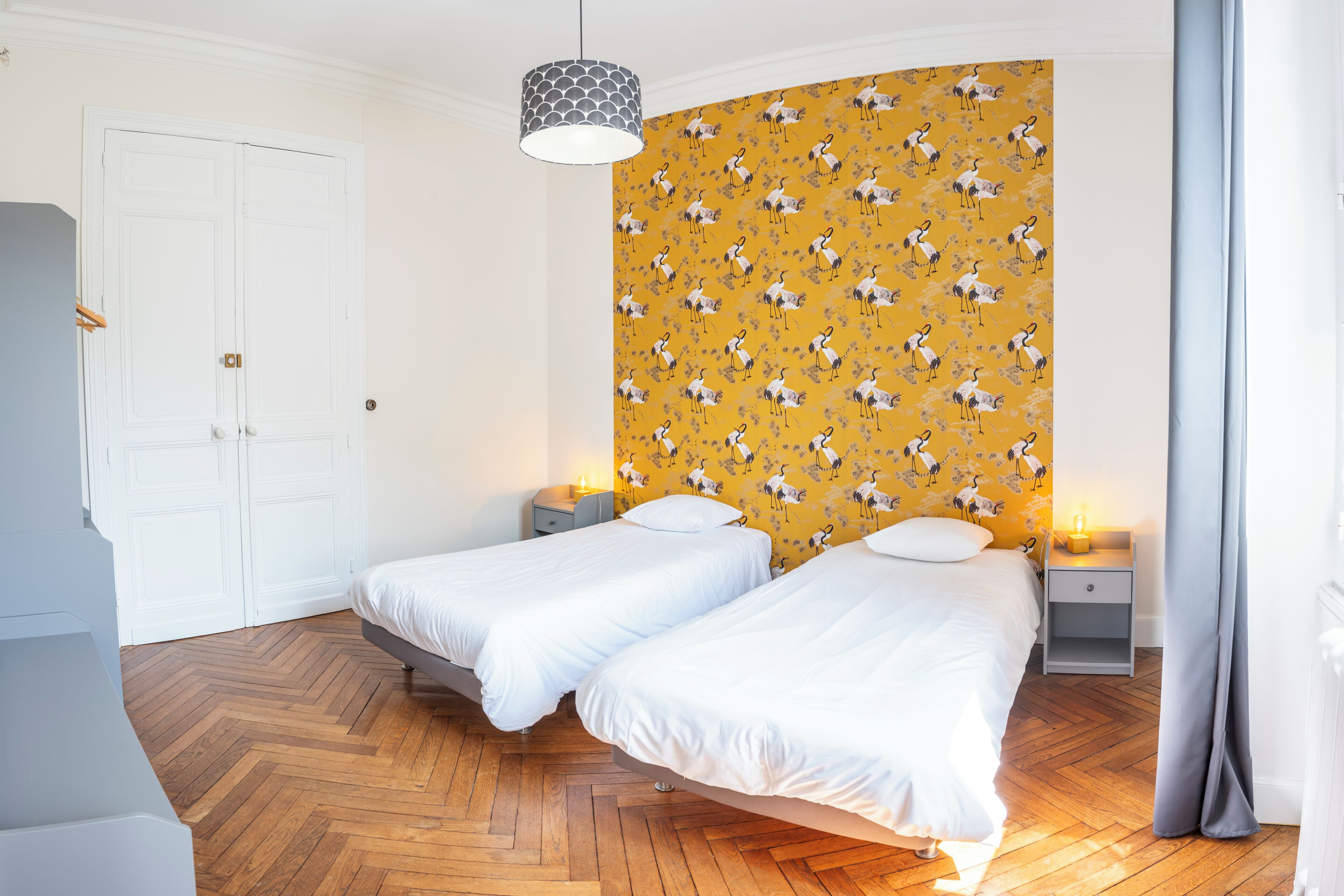 A bedroom with two beds, wooden flooring, a patterned wallpaper, and a white door.