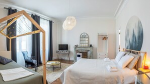 A bedroom with a large bed, a small desk, a television, and a fireplace.