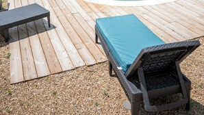 A swimming pool with a wooden deck, a lounge chair, and a bench.