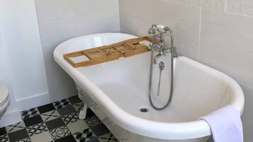 A bathroom with a white bathtub, a wooden tray, a showerhead, and patterned floor tiles.
