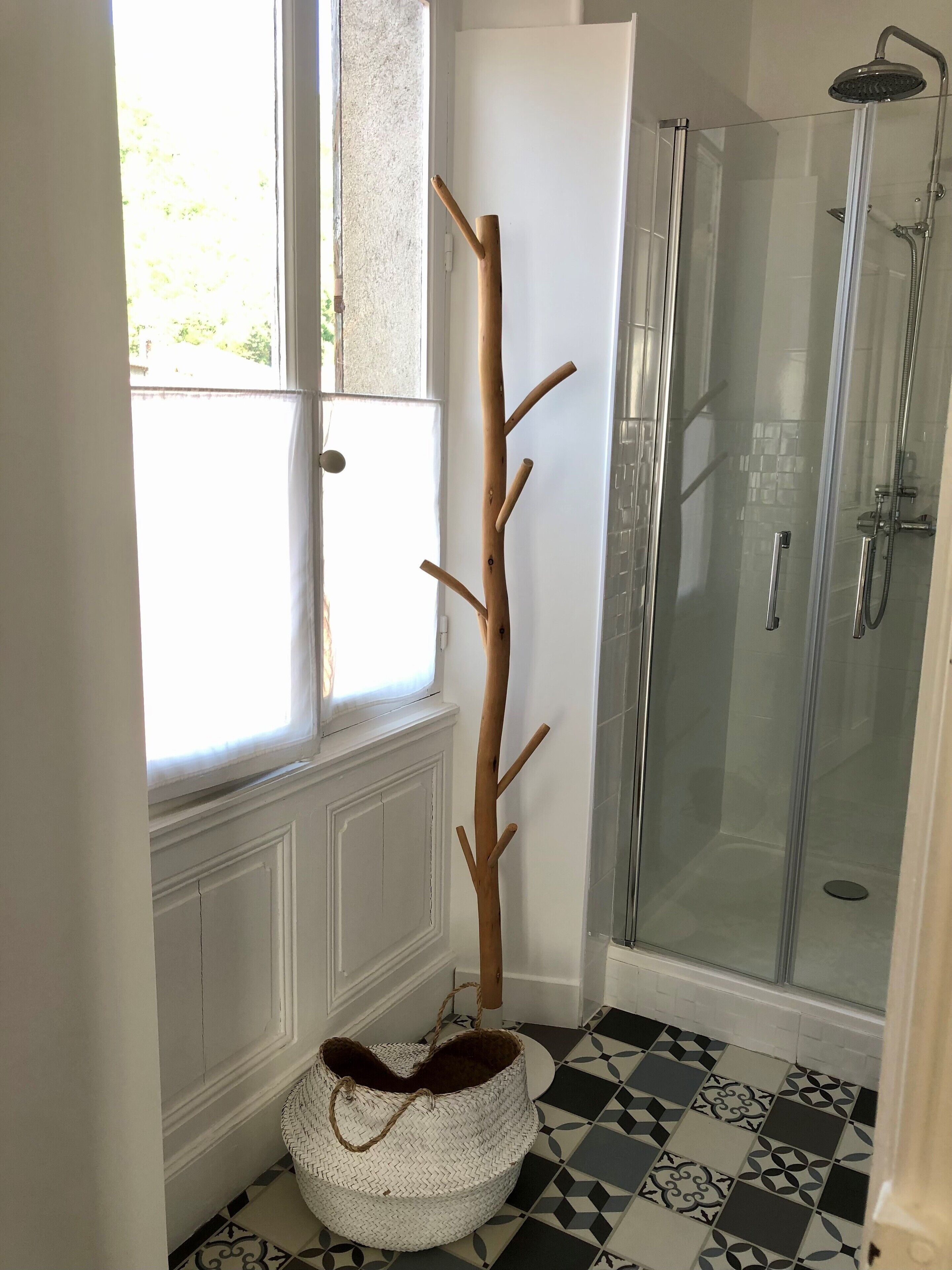 A bathroom with a shower, a wooden coat rack, a woven basket, and patterned floor tiles.
