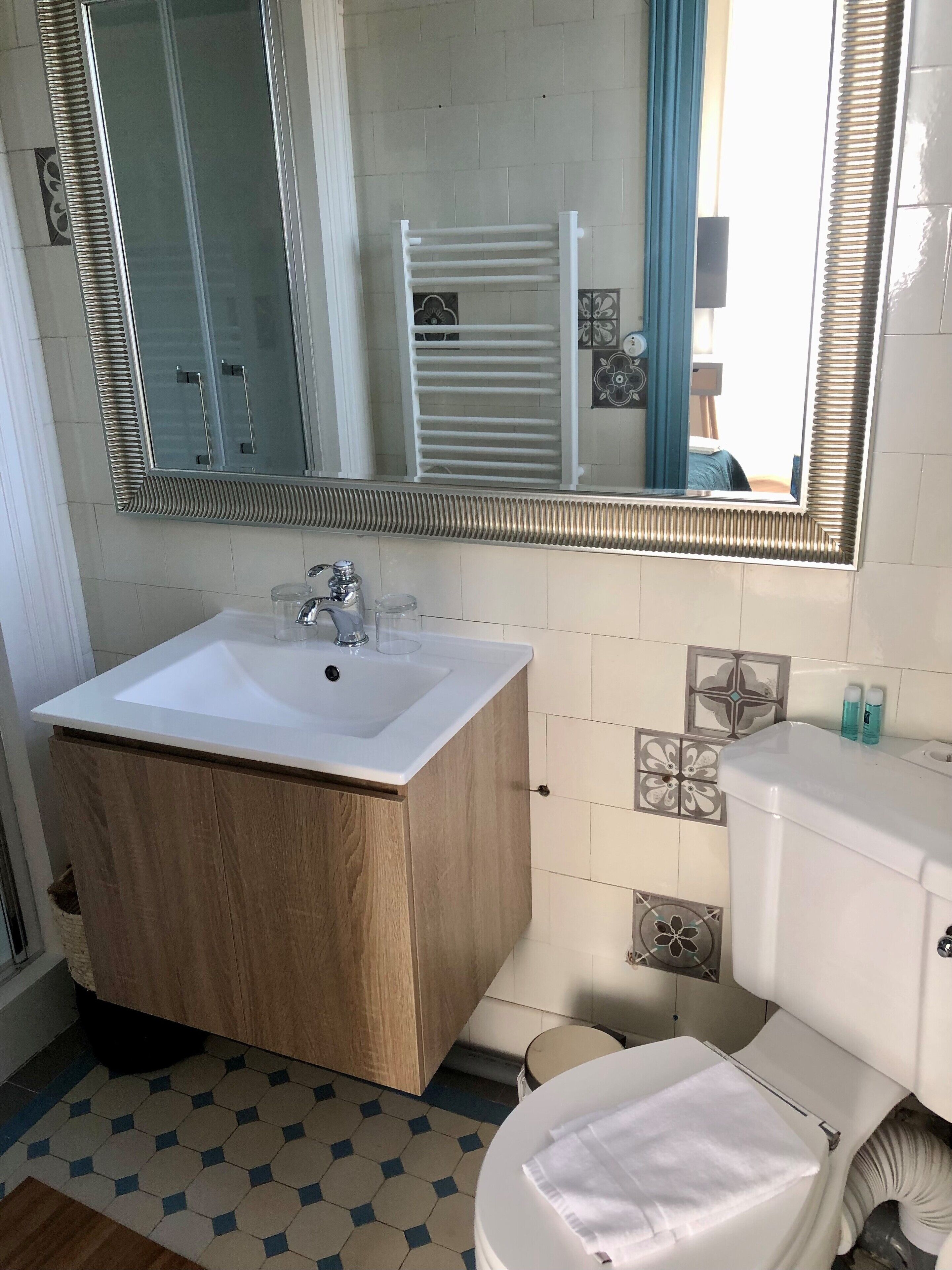 Un baño con tocador de madera, un lavabo blanco, un espejo, un inodoro y un perchero para toallas.
