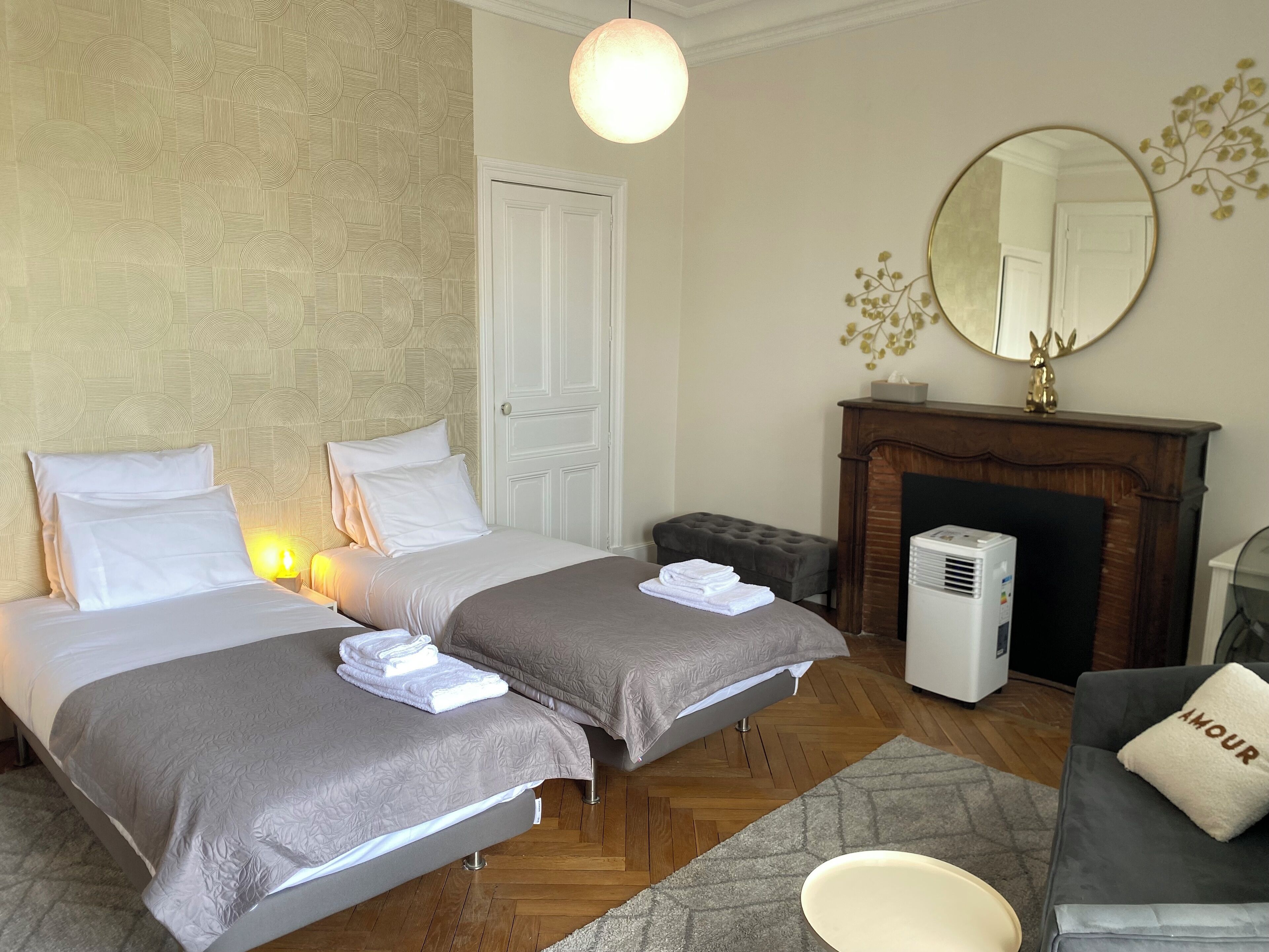 A hotel room with two beds, a fireplace, a mirror, and a sofa.