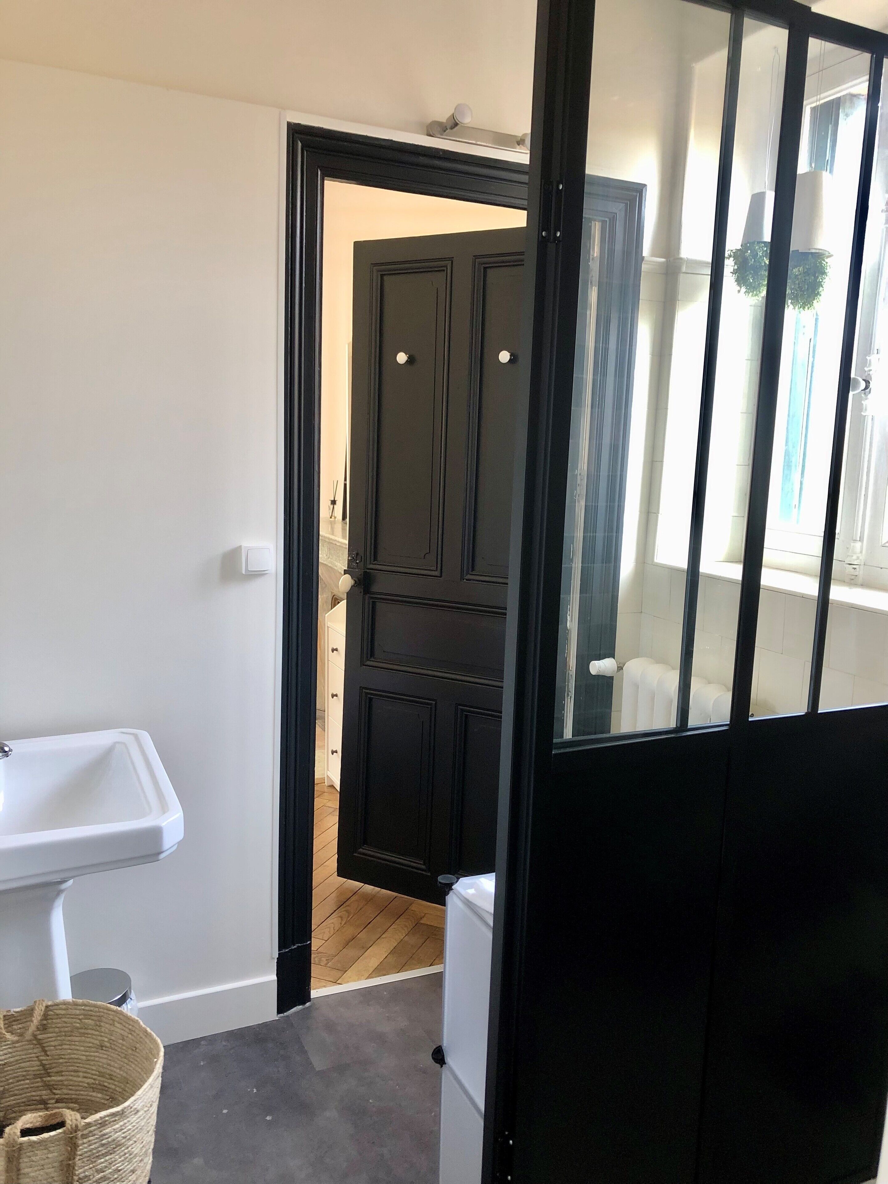 A narrow hallway with a white sink, a dark wooden door, and a window with blinds.