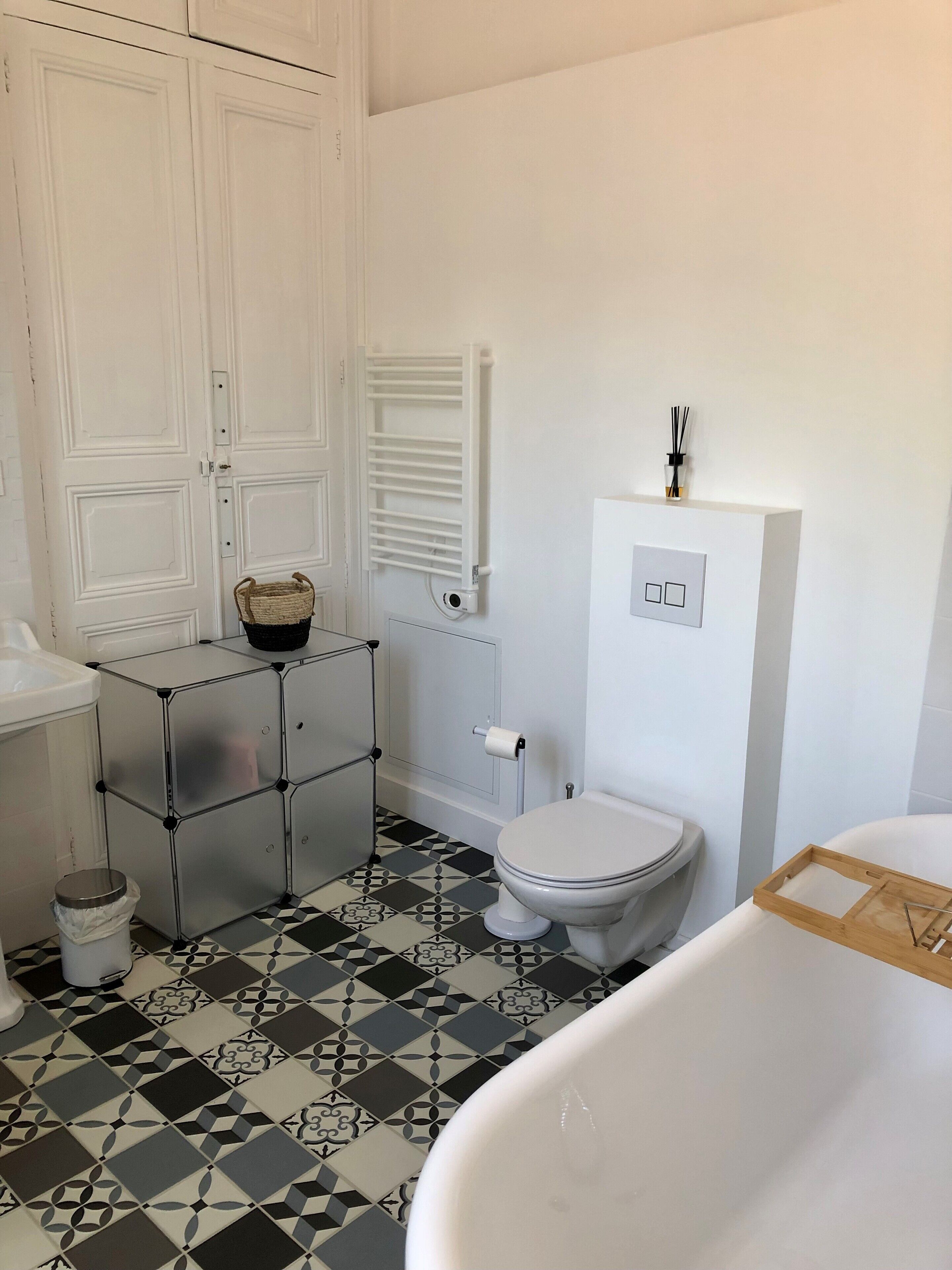 A bathroom with a white toilet, a white bathtub, a metal cabinet, a patterned floor, and a white wall with a radiator.