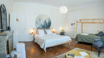 A bedroom with a bed, bedside tables, a nightstand, a chair, a table, a painting, and a hanging light fixture.
