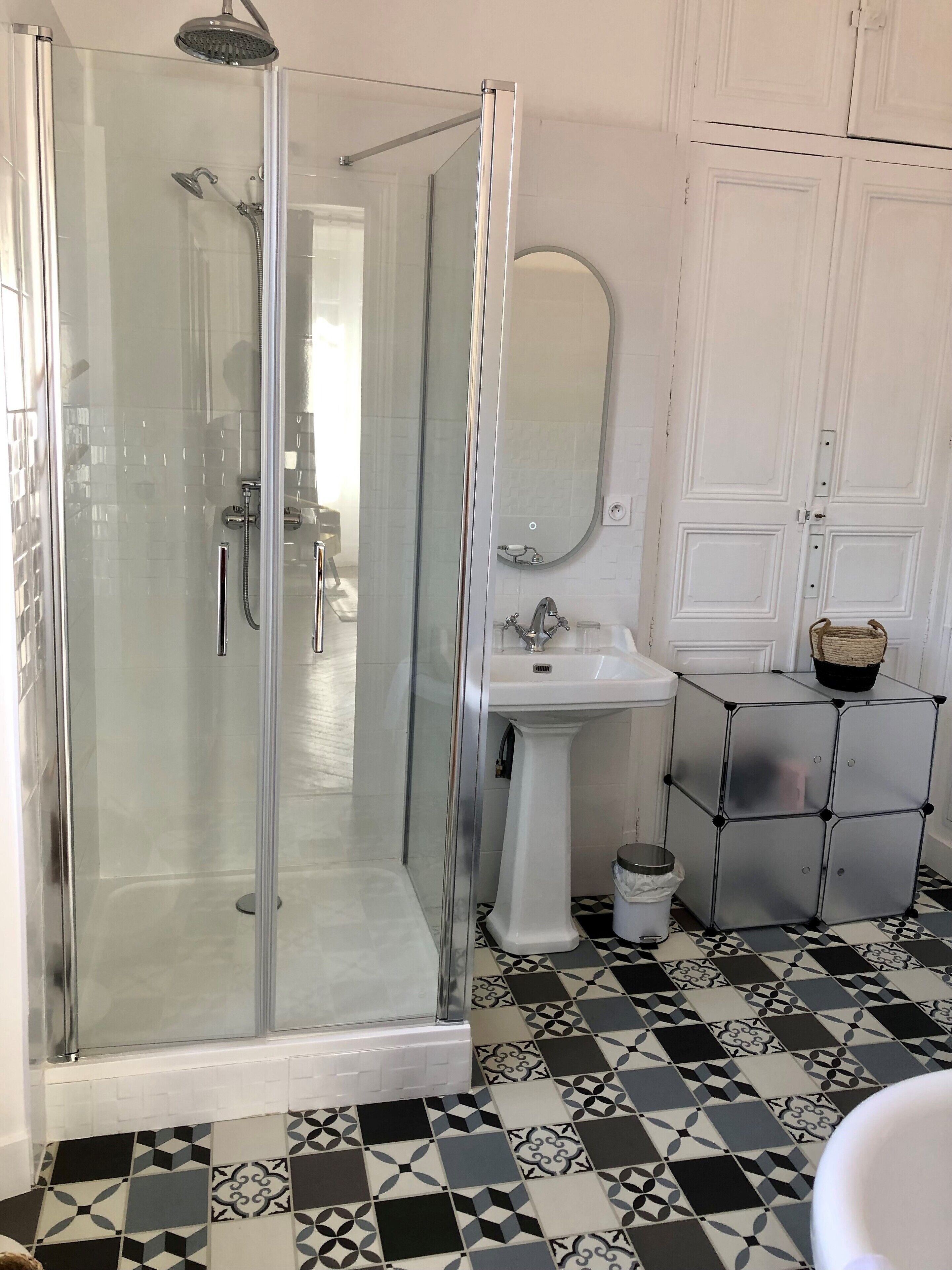A bathroom with a glass-enclosed shower, a pedestal sink, and a tiled floor.