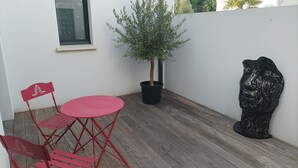 A small patio with a red metal table and chairs, a potted tree, and a black sculpture. - Single-storey house Royan 8 pers - Heated swimming pool in summer - Pontaillac beach (VAUX SUR MER)