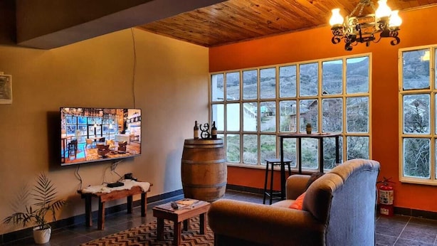 Un salon chaleureux, doté d’un téléviseur, de meubles en bois et de grandes fenêtres offrant une vue sur l’extérieur.