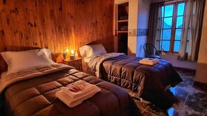 Une pièce confortable avec deux lits, des murs en bois, une fenêtre avec des rideaux et une table de chevet avec une lampe.