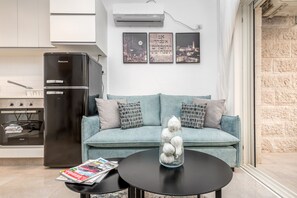 A modern living room with a sofa, a coffee table with magazines, a black refrigerator, and a wall with three framed pictures.