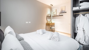 A hotel room with a bed, a vanity with a mirror, a robe rack, and a wall-mounted artwork. - One BDR with a Huge Terrace (Jerusalem)