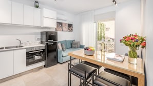 A modern kitchen with white cabinets, a black refrigerator, and a glass dining table with black chairs. - One BDR with a Huge Terrace (Jerusalem)