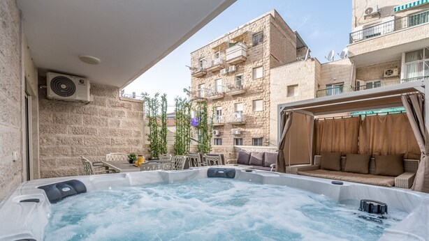 A hot tub with a stone wall backdrop, outdoor furniture, and a building with balconies and satellite dishes. - One BDR with a Huge Terrace (Jerusalem)
