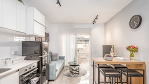 A modern kitchen with white cabinets, a stainless steel refrigerator, and a dining area with a wooden table and bar stools. - One BDR with a Huge Terrace (Jerusalem)