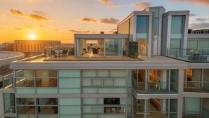 Un moderno edificio de varios pisos con una terraza en la azotea, amplias ventanas y una vista despejada del atardecer.