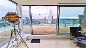 Habitación con ventanas amplias que ofrecen vistas a la ciudad, un telescopio y un sillón de cuero negro.