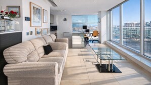 Una sala de estar moderna con un sofá, una mesa de centro de vidrio y vistas a la ciudad a través de amplios ventanales.