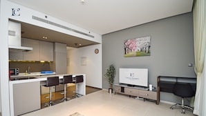 A modern hotel room with a kitchenette, a dining area with bar stools, a flat-screen TV, a potted plant, and a large window with curtains. - Brand New 1BR Apartment West Avenue Marina - CLN (Dubai)