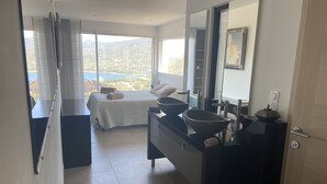 A modern bedroom with a large bed, a bathroom with a black vanity and a large mirror, and a view of a mountainous landscape through large windows. - Villa Propriano 6 to 8 people VILLA WITH POOL AND SEA VIEW (VIGGIANELLO)