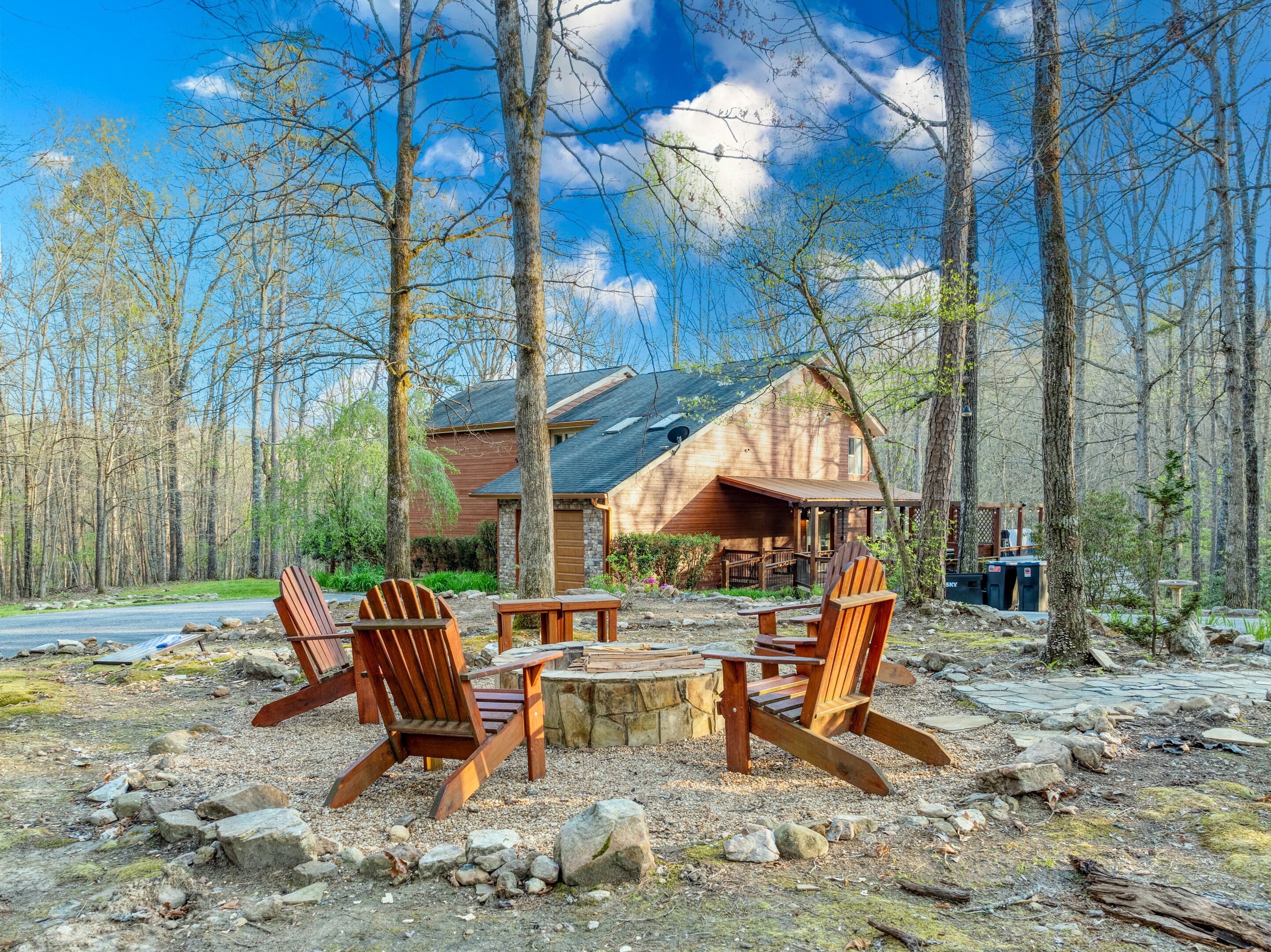 A cabin with a stone fire pit, two Adirondack chairs, and a view of the forest.