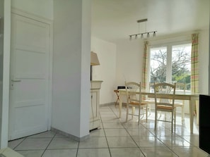 A room with a white door, a dining table with chairs, a lamp, and a window with curtains.