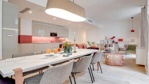 Uma cozinha moderna com armários brancos, uma ilha central e uma área de jantar com uma mesa comprida e cadeiras.