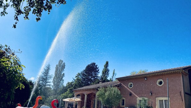 A swimming pool with inflatable swan and rainbow floats, surrounded by a building with a tiled roof and a garden. - NO, AVAILABLE AD BEING REMOVED (Ceilhes-et-Rocozels)