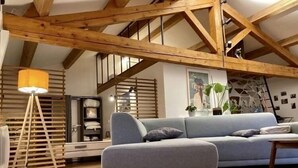 A modern loft-style living room with exposed wooden beams, a grey sofa, and a floor lamp. - NO, AVAILABLE AD BEING REMOVED (Ceilhes-et-Rocozels)