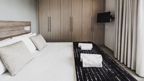 A modern hotel room with a large bed, a flat-screen TV mounted on the wall, and a wooden wardrobe. - Almyra (Chios)