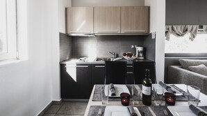 A modern kitchen with dark cabinetry, a dining area with a table set for two, and a view of the outdoors through a window. - Almyra (Chios)