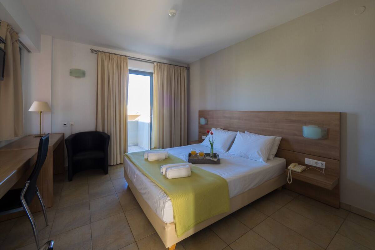 A hotel room with a bed, bedside table, lamp, chair, and a desk.