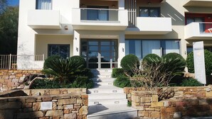 A modern two-story hotel with a stone facade, large windows, and a central entrance with steps. - Almyra (Chios)