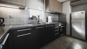 A modern kitchen with dark cabinetry, a stainless steel sink, and a built-in oven. - Almyra (Chios)